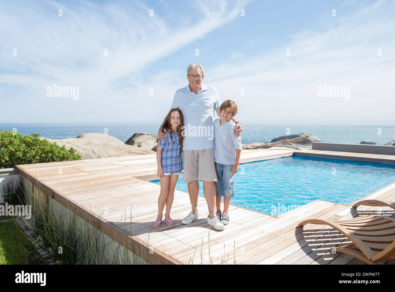 Older man and grandchildren smiling by pool Stock Photo