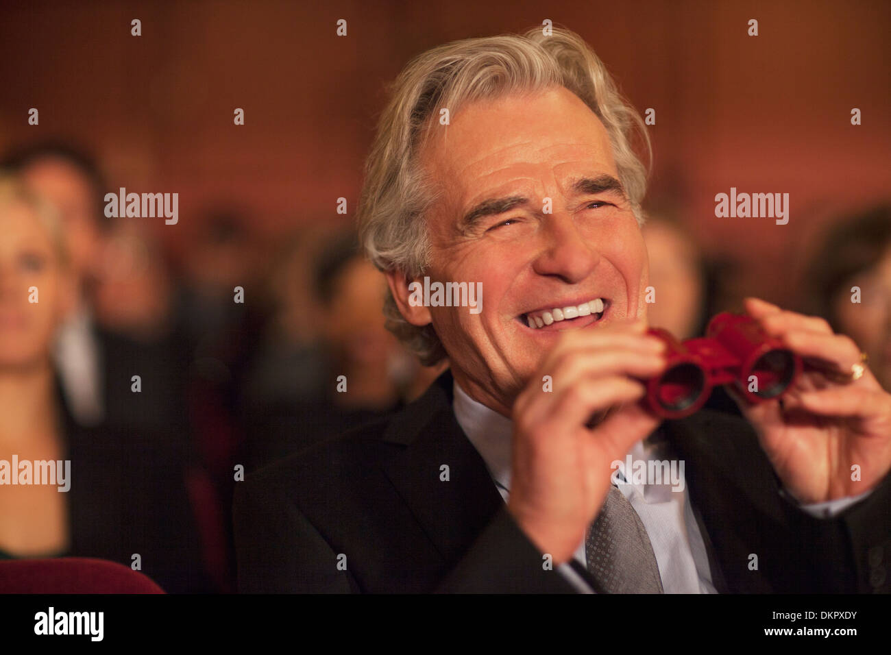 Man with opera glasses laughing in theater audience Stock Photo