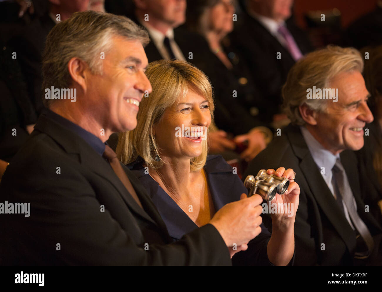 Happy couple holding opera glasses in theater audience Stock Photo