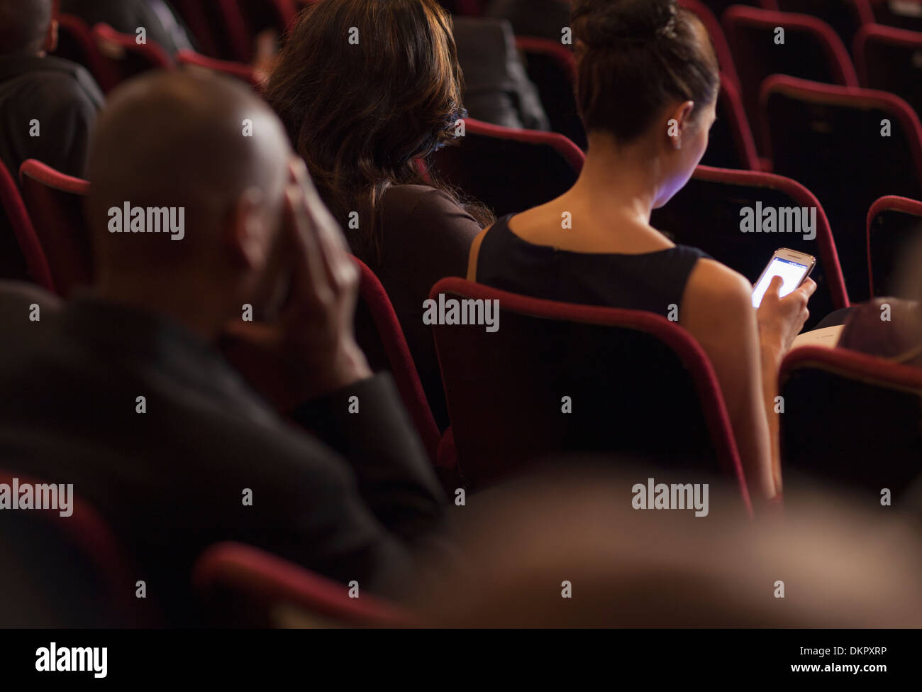 Rear view of woman using cell phone in theater audience Stock Photo