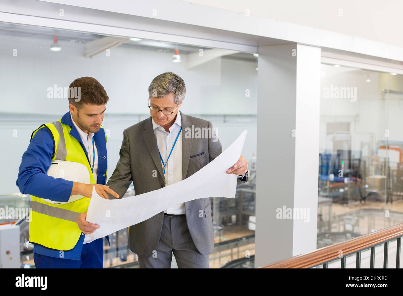 Supervisor and worker reading blueprints in factory Stock Photo