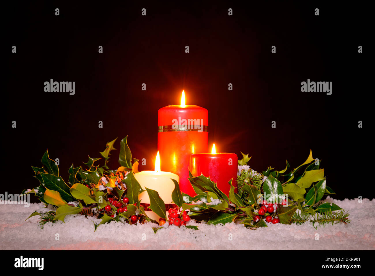 Christmas still life of three candles on snow surrounded by a fresh green holly, ivy and spruce garland Stock Photo