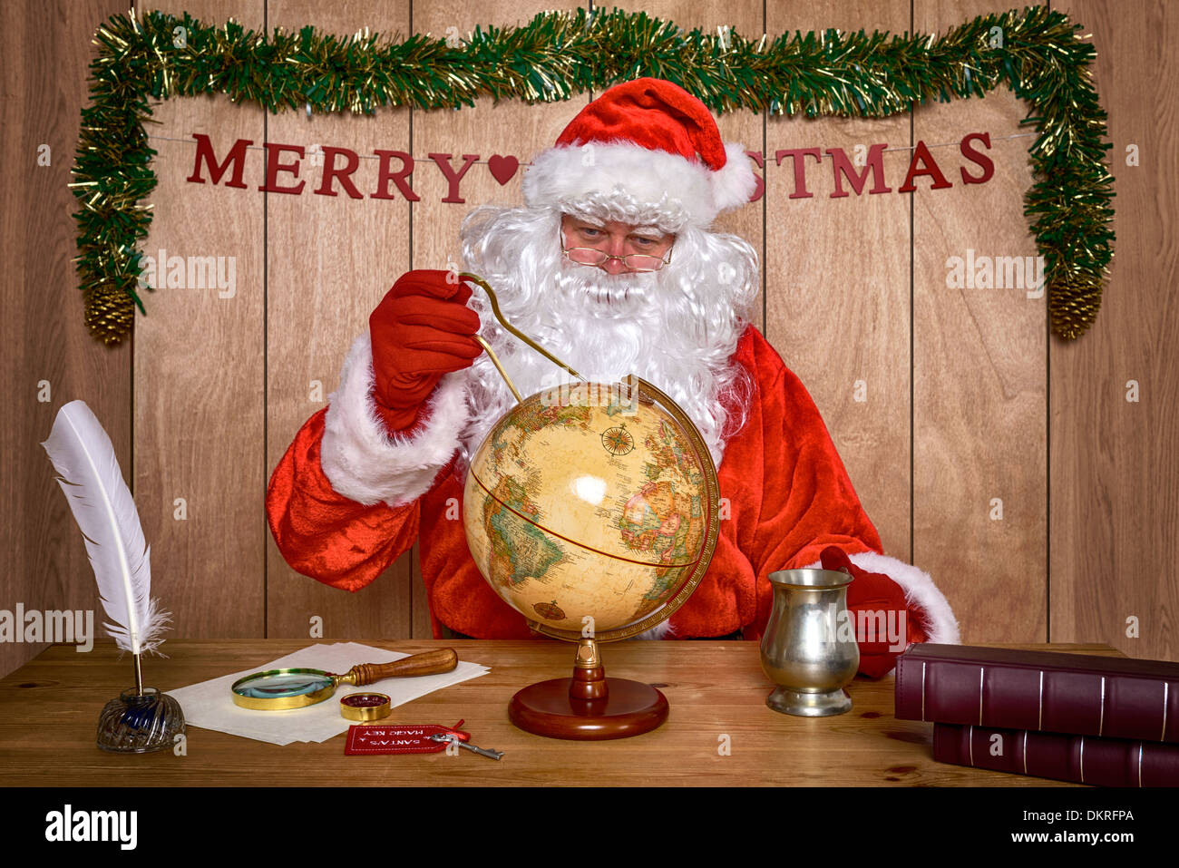 Santa sat at his desk in the North Pole looking at a world globe as he plans his route to deliver all the toys on Christmas Eve. Stock Photo