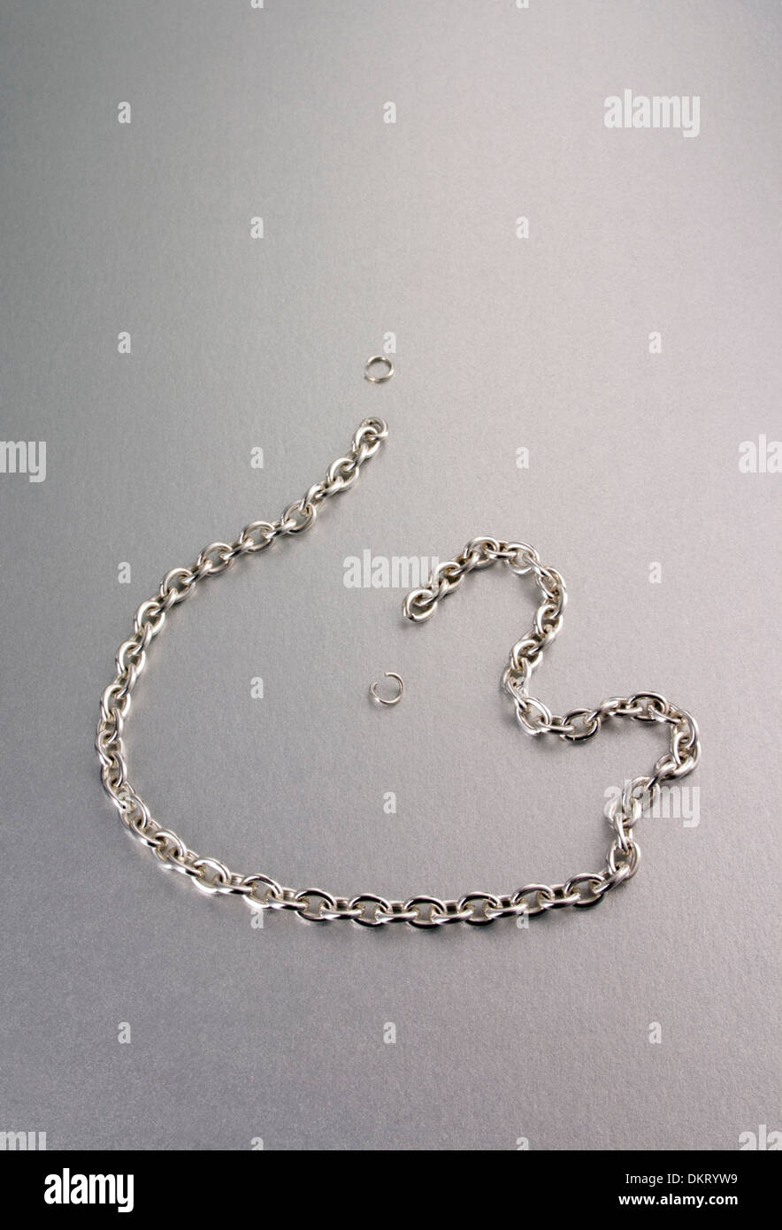 A silver link chain, broken with missing links on a silver background. Stock Photo