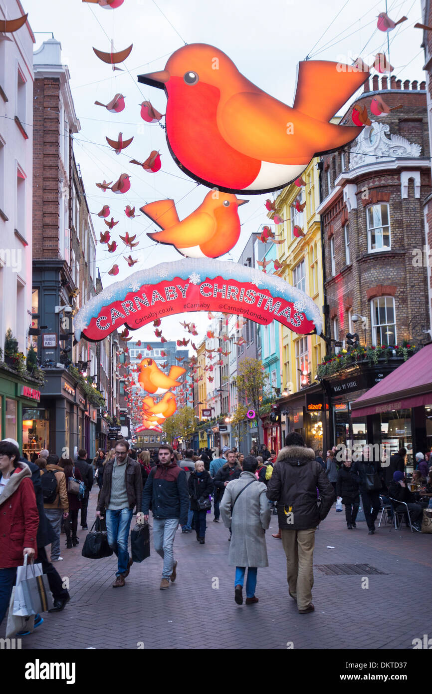The 'Year of the Robin' Christmas decorations hang above Carnaby Street, London, England as people shop for presents Stock Photo