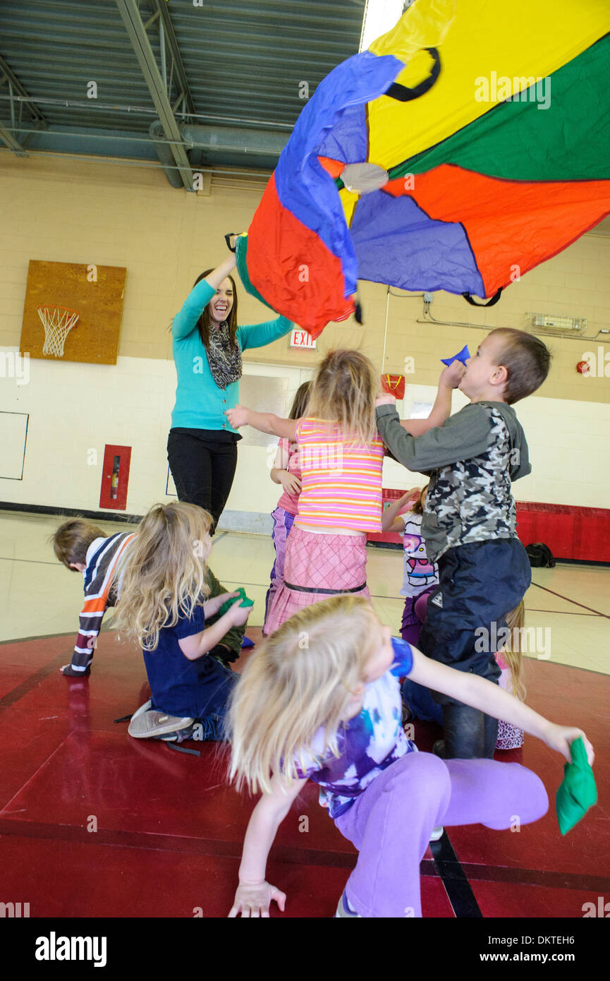 Pre-school children playing with rainbow parachute in gym Stock Photo