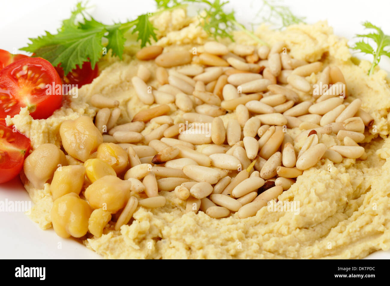 Hummus and lightly roasted pine-nuts dip, garnished with cherry tomatoes and young salad leaves, viewed close-up Stock Photo