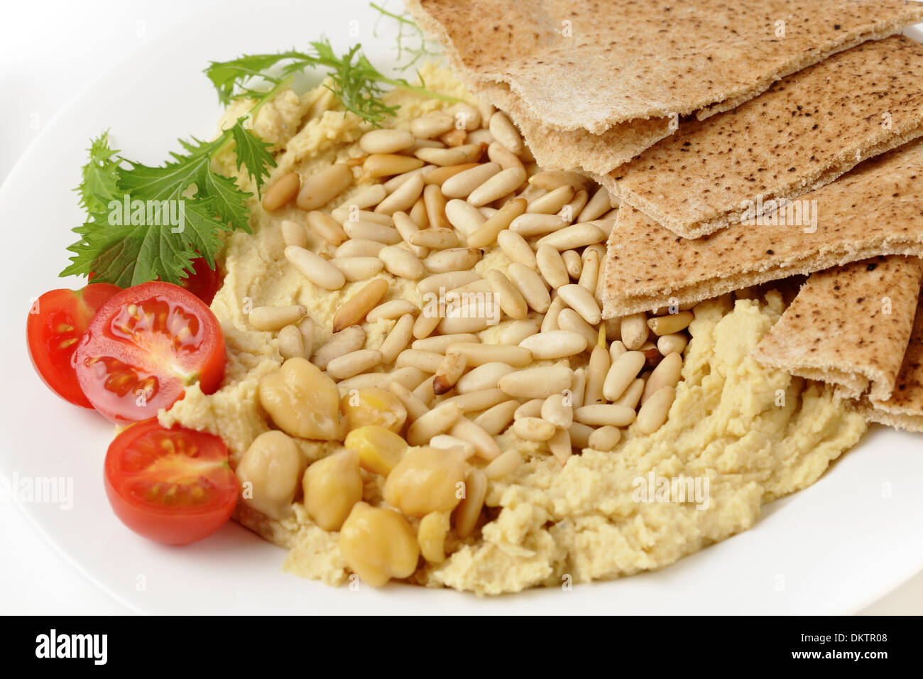 Hummus and lightly roasted pine-nuts dip, garnished with cherry tomatoes and young salad leaves, viewed close-up Stock Photo