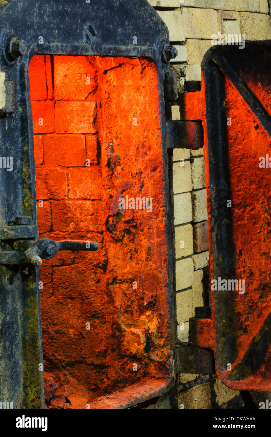 Cast-iron door of a large oven kiln incinerator made from bricks, with the glow of the fire inside. Stock Photo