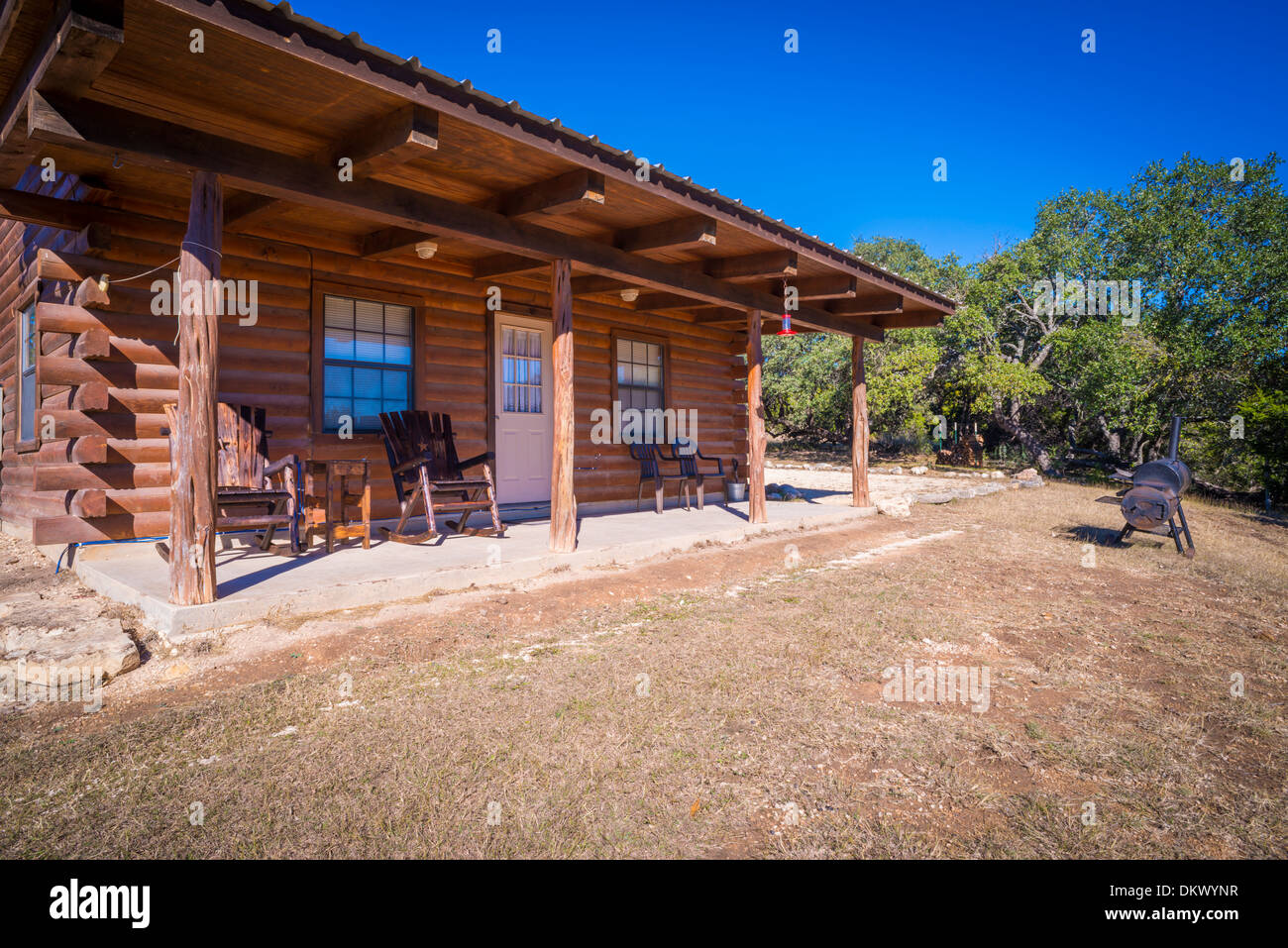 Exterior of rustic farm log house with wooden rocking chairs on the fron deck. Barbecue smoker in the front yard. Texas, USA. Stock Photo