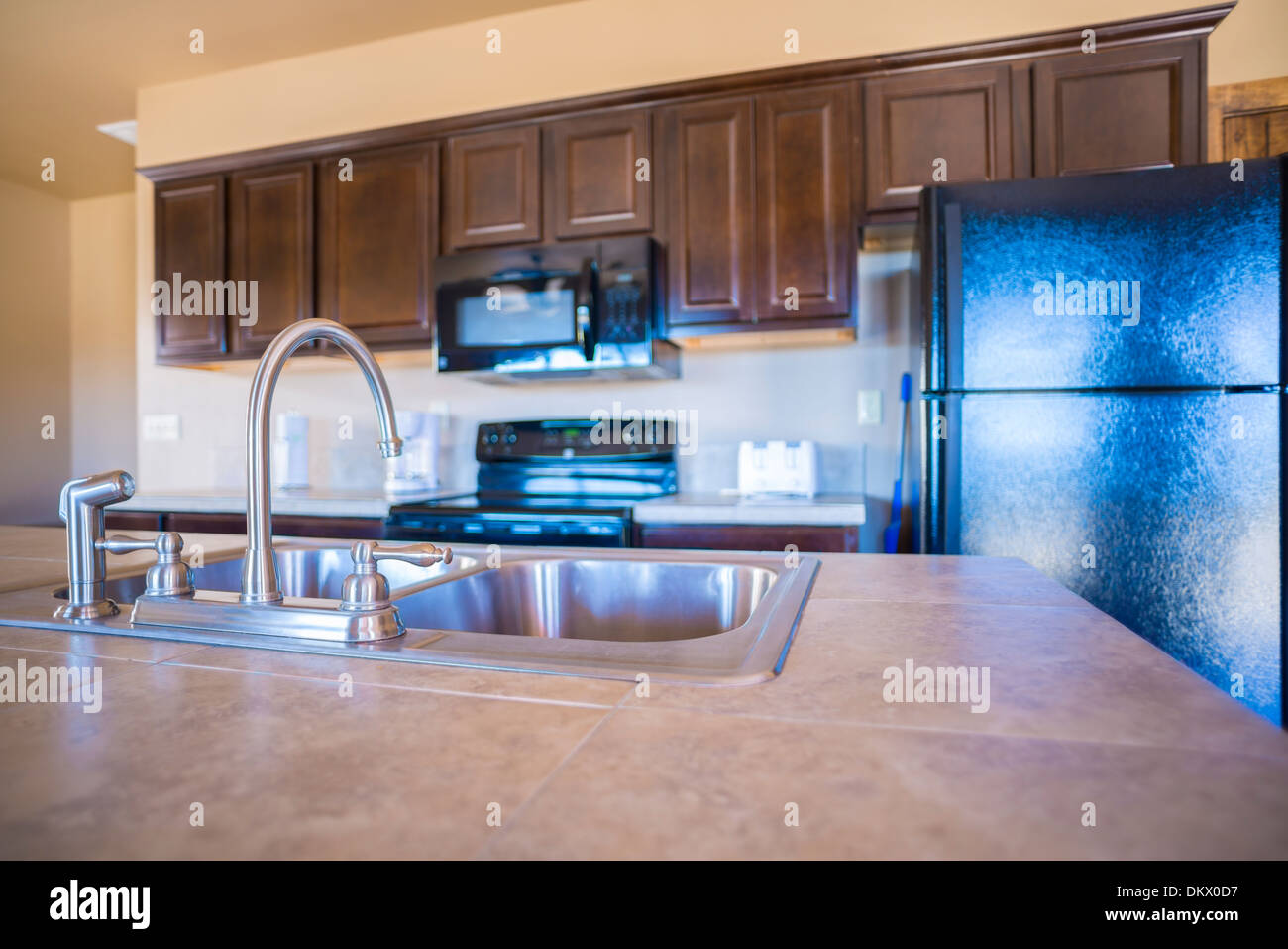 Kitchen Interior. Close up of double sink in kitchen with wall cabinets, range, microwave oven and refrigerator in background Stock Photo