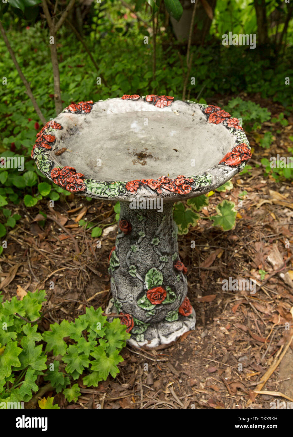 Ornate concrete bird bath with decoration of red roses and green leaves - an attractive feature to attract birds to the garden Stock Photo