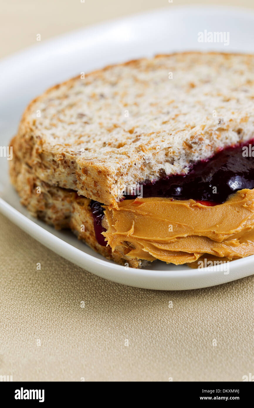 Closeup vertical photo of peanut butter and jelly sandwich, cut in half, inside white plate on textured table cloth underneath Stock Photo