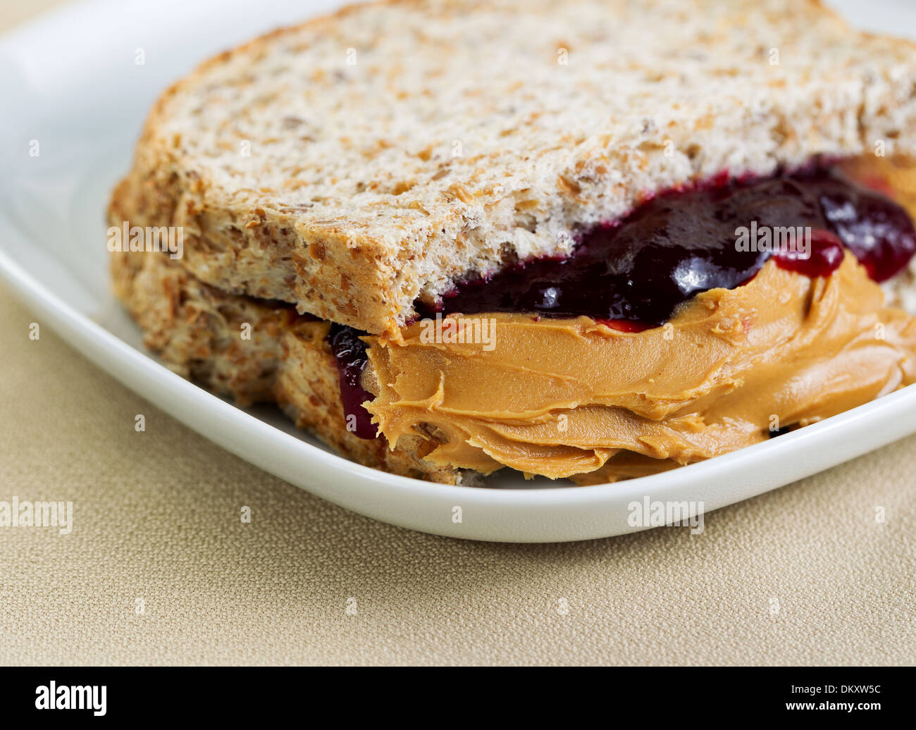 Closeup horizontal photo of a peanut butter and jelly sandwich cut in half, inside white plate on textured table cloth Stock Photo