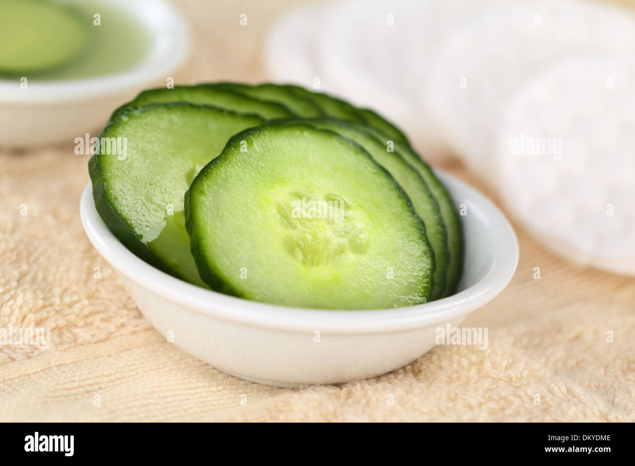 Cucumber slices used as natural moisturizer pads for the eyes in a bowl on towel Stock Photo