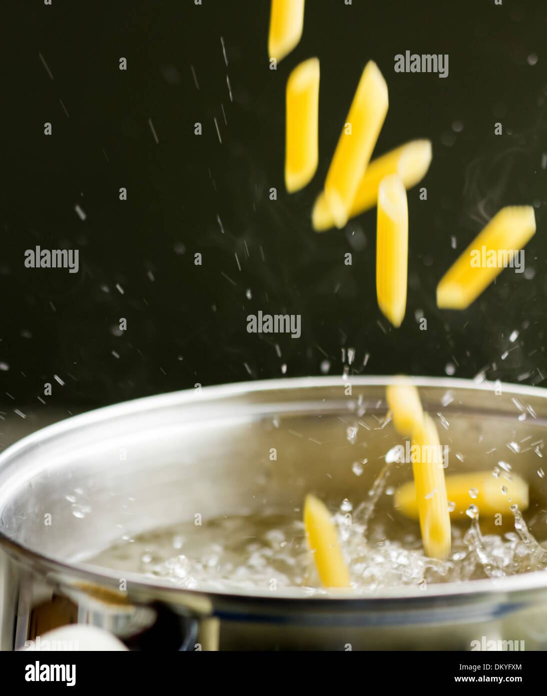 Dropping dry penne pasta tubes into boiling water Stock Photo