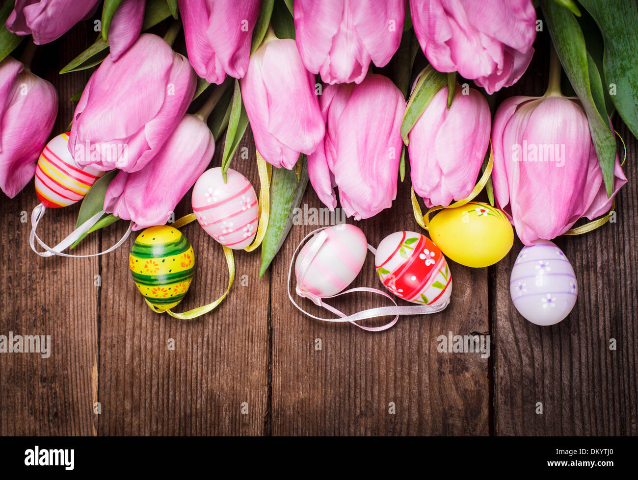 Tulips and eggs border over wooden backdrop. Easter decorations. Stock Photo