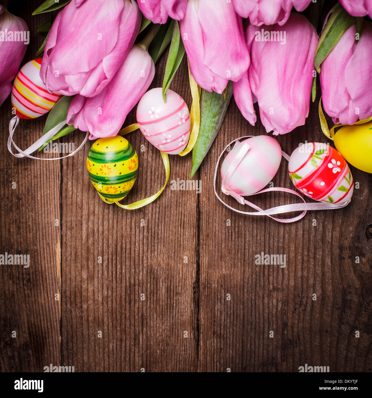 Tulips and eggs border over wooden backdrop. Easter decorations. Stock Photo
