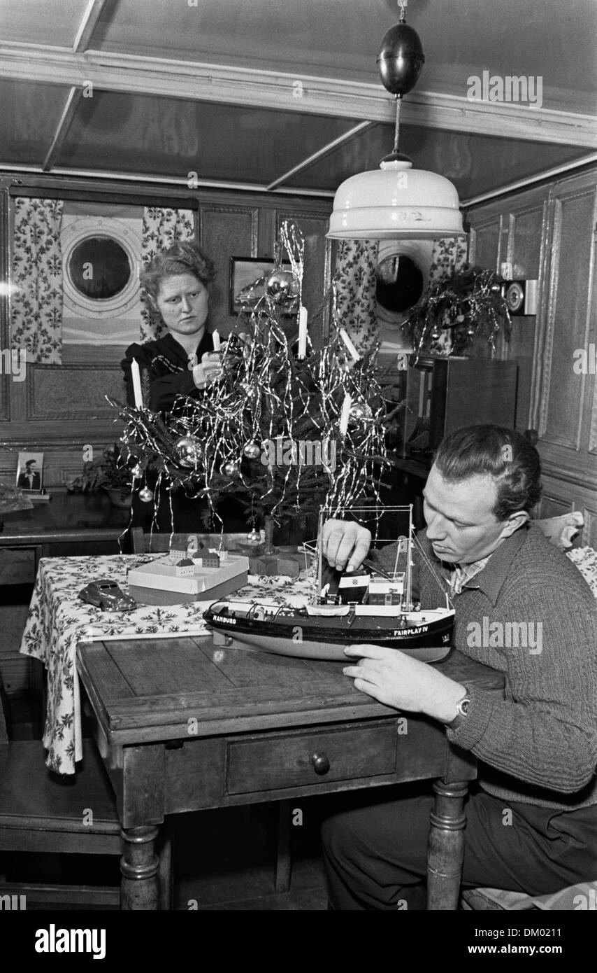 A man does handicrafts on a ship model, a woman decorates a small Christmas tree in the background, undated photograph (December 1955). Photo: Deutsche Fotothek/Erich Höhne, Erich Pohl Stock Photo