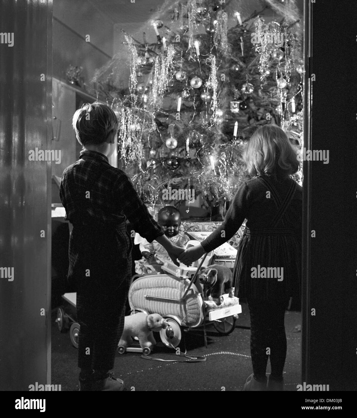 Brother and sister hold hands while they look at the decorated Christmas tree and at Christmas presents, 24 December 1961. Photo: Heinz Junge Stock Photo