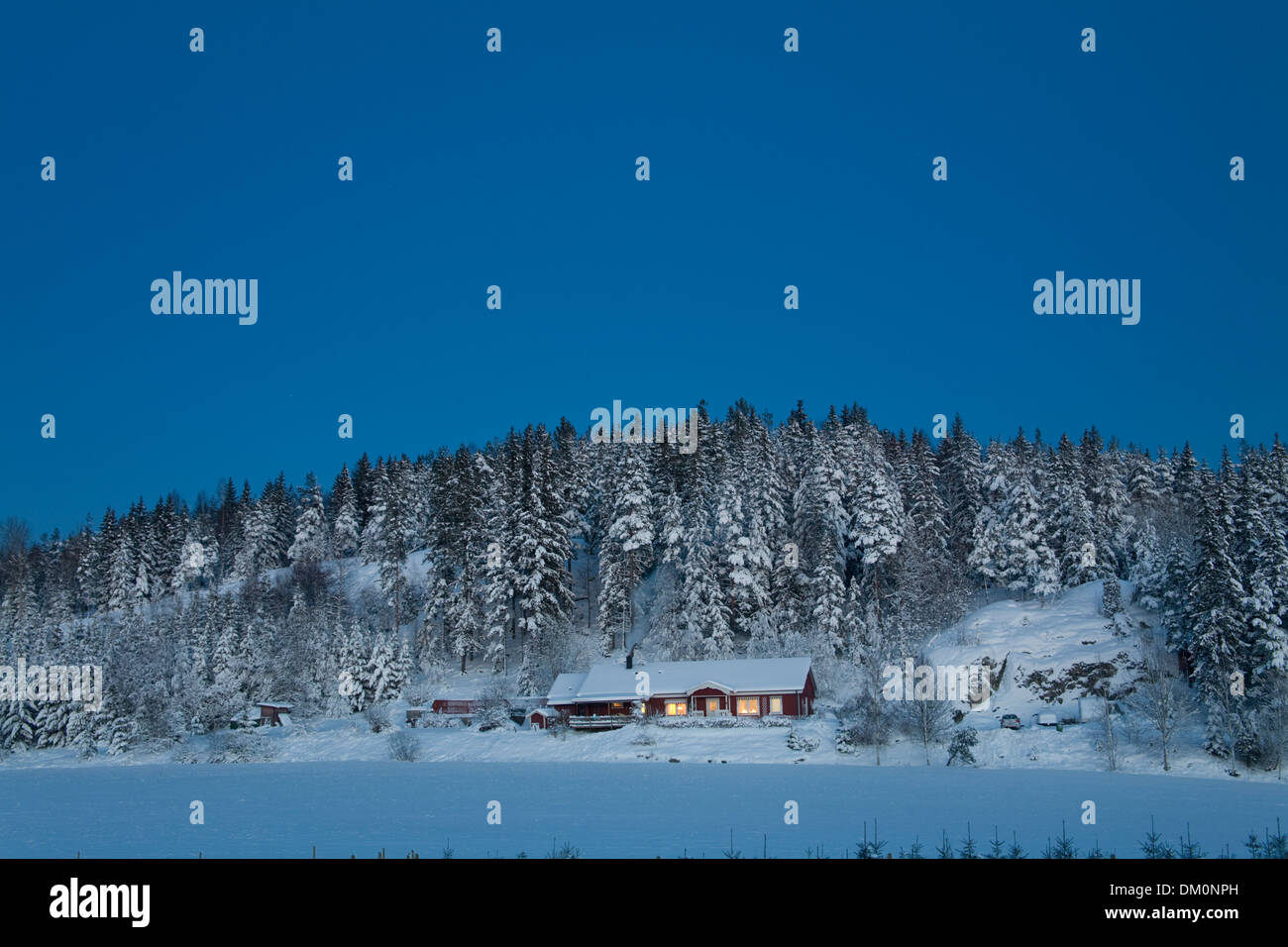 Cold Blue Evening light over snowy landscape with illuminated house Stock Photo