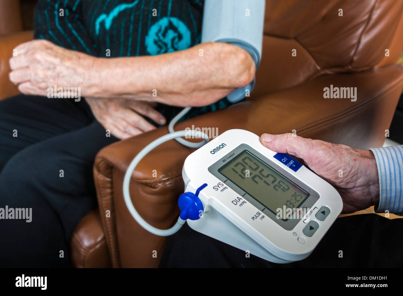 Close up of elderly couple checking their own blood-pressure using a digital blood pressure monitor in living room at home Stock Photo