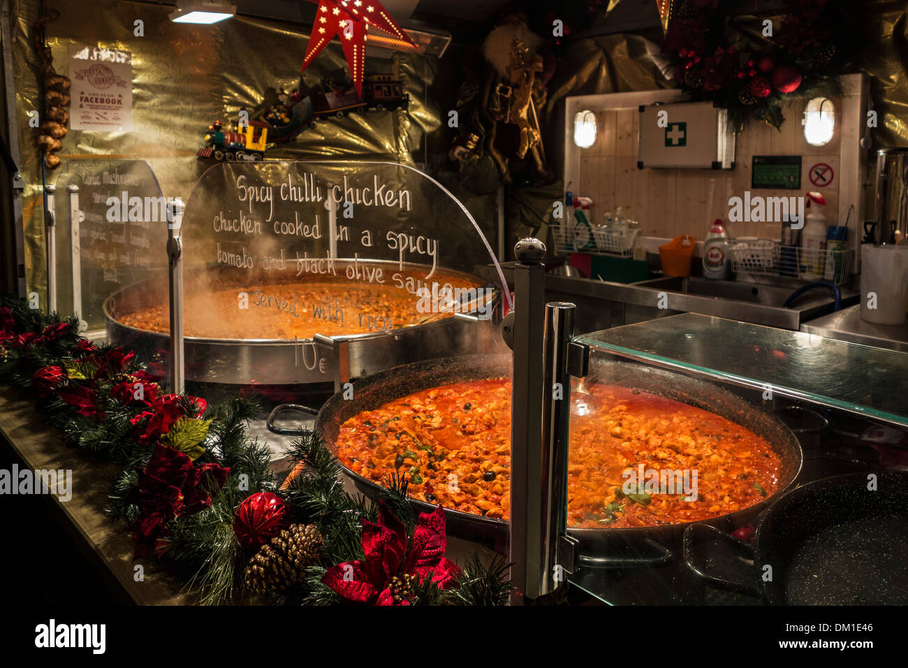Large pans with simmering spicy chilli chicken for sale in stall during evening Christmas market in winter Stock Photo