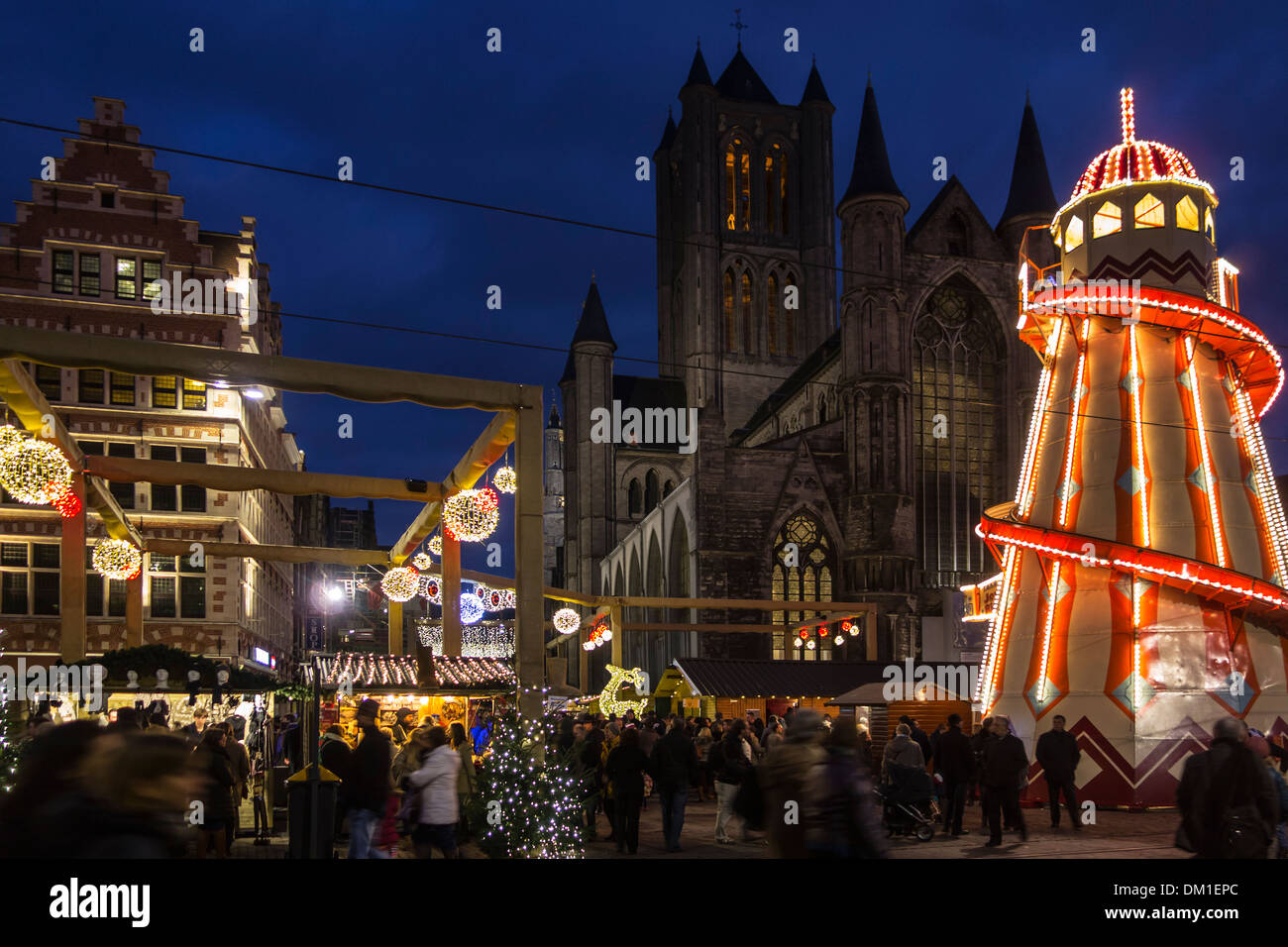 Illuminated helter skelter and people shopping at evening Christmas market in winter, Korenmarkt / Corn Market, Ghent, Belgium Stock Photo