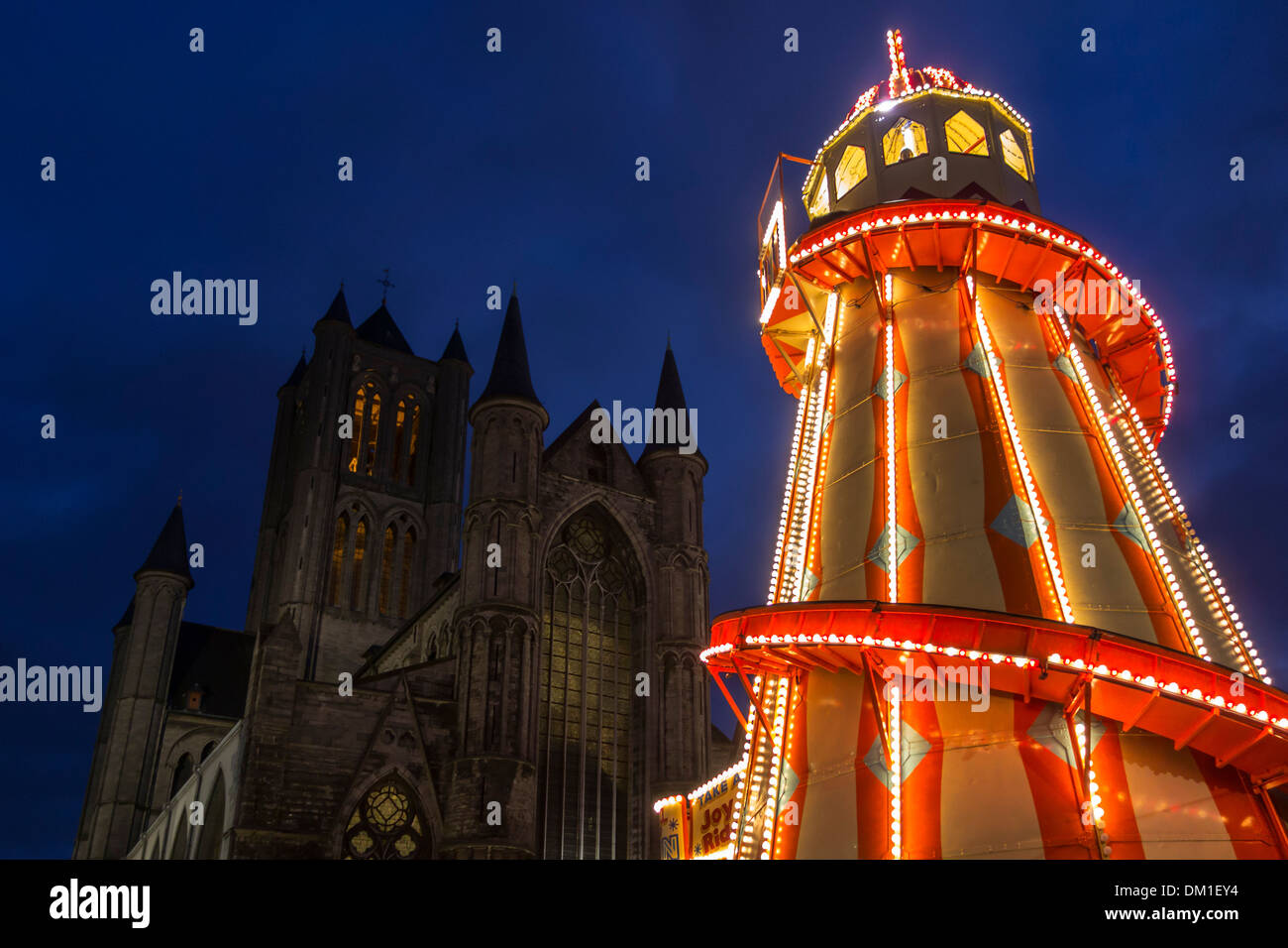 Illuminated helter skelter at evening Christmas market and Saint Nicholas church in winter, Korenmarkt, Ghent, Belgium Stock Photo