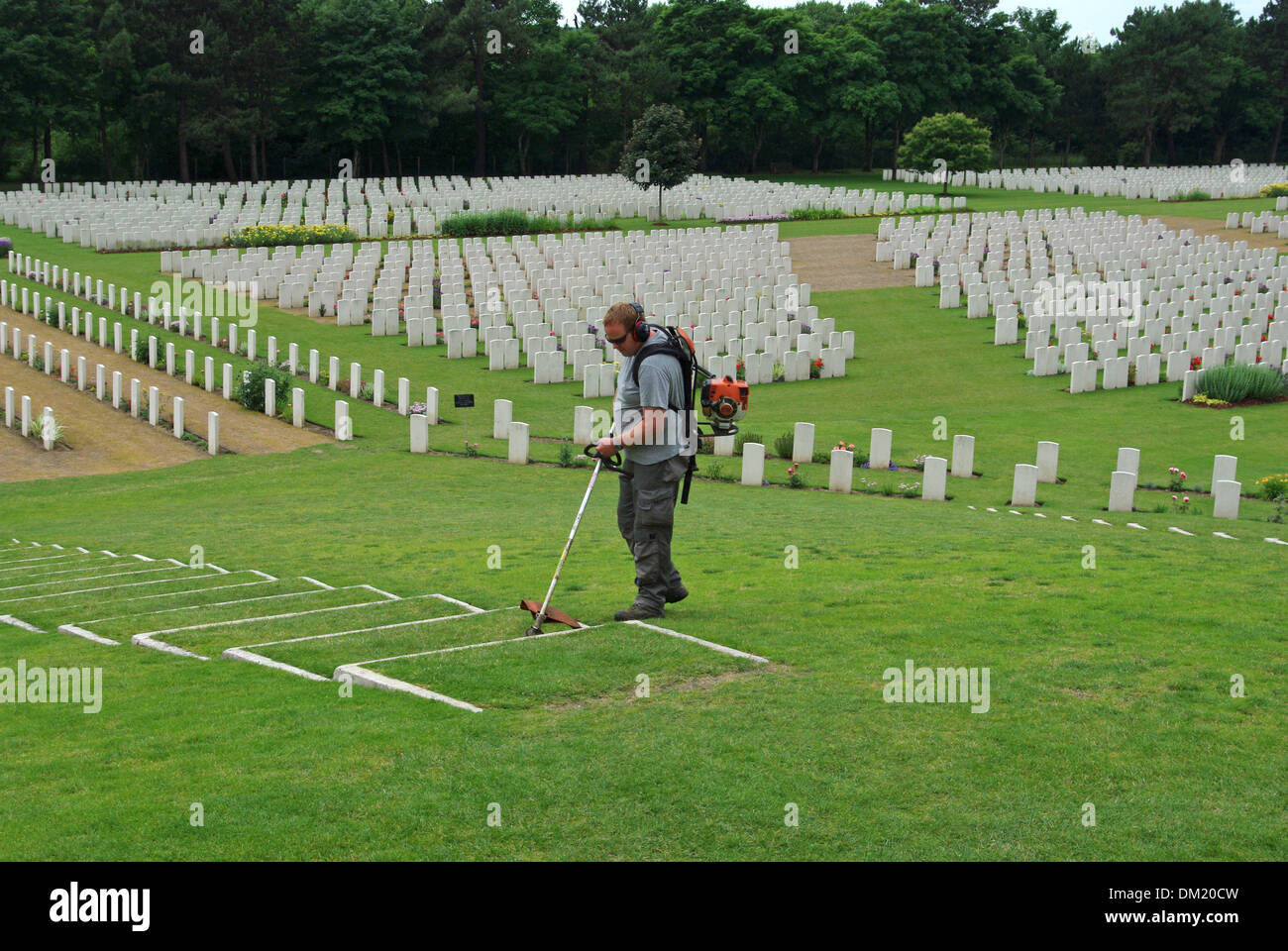 Male gardener lawn cutting at the WW1 Etaples Military Cemetery, rows of war graves in the background Stock Photo