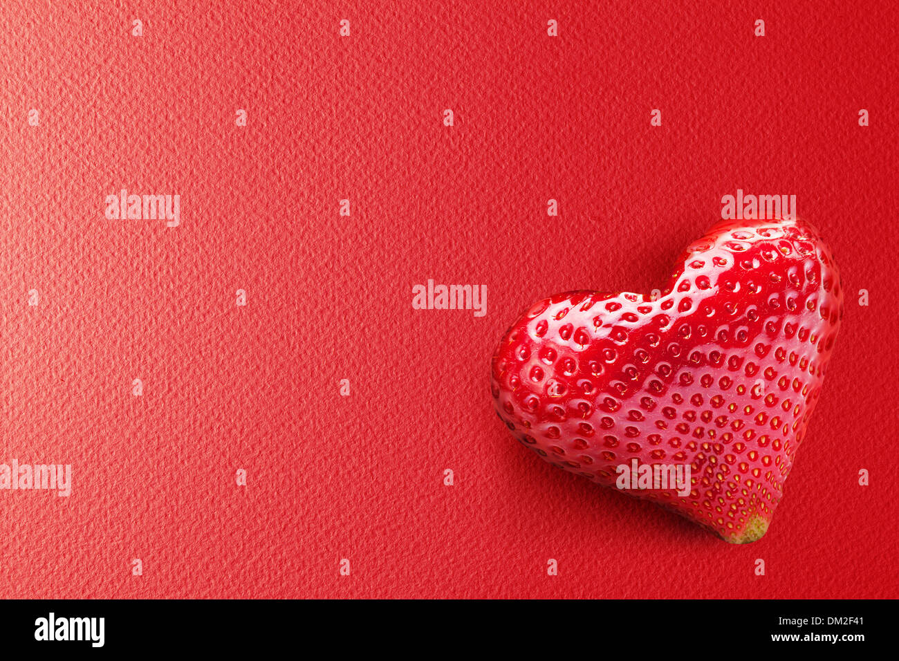 One rich strawberry fruit in form of heart on a red background. Stock Photo