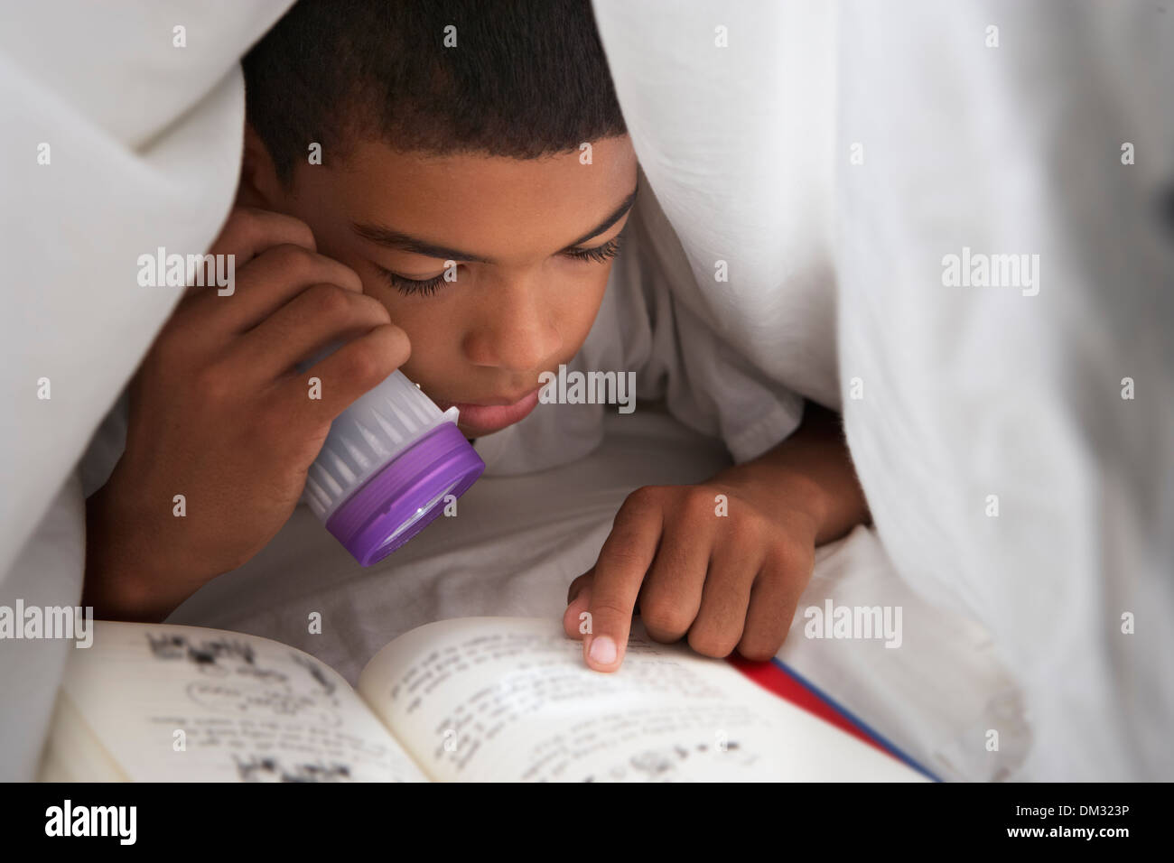 Boy Reading Book With Torch Under Duvet Stock Photo