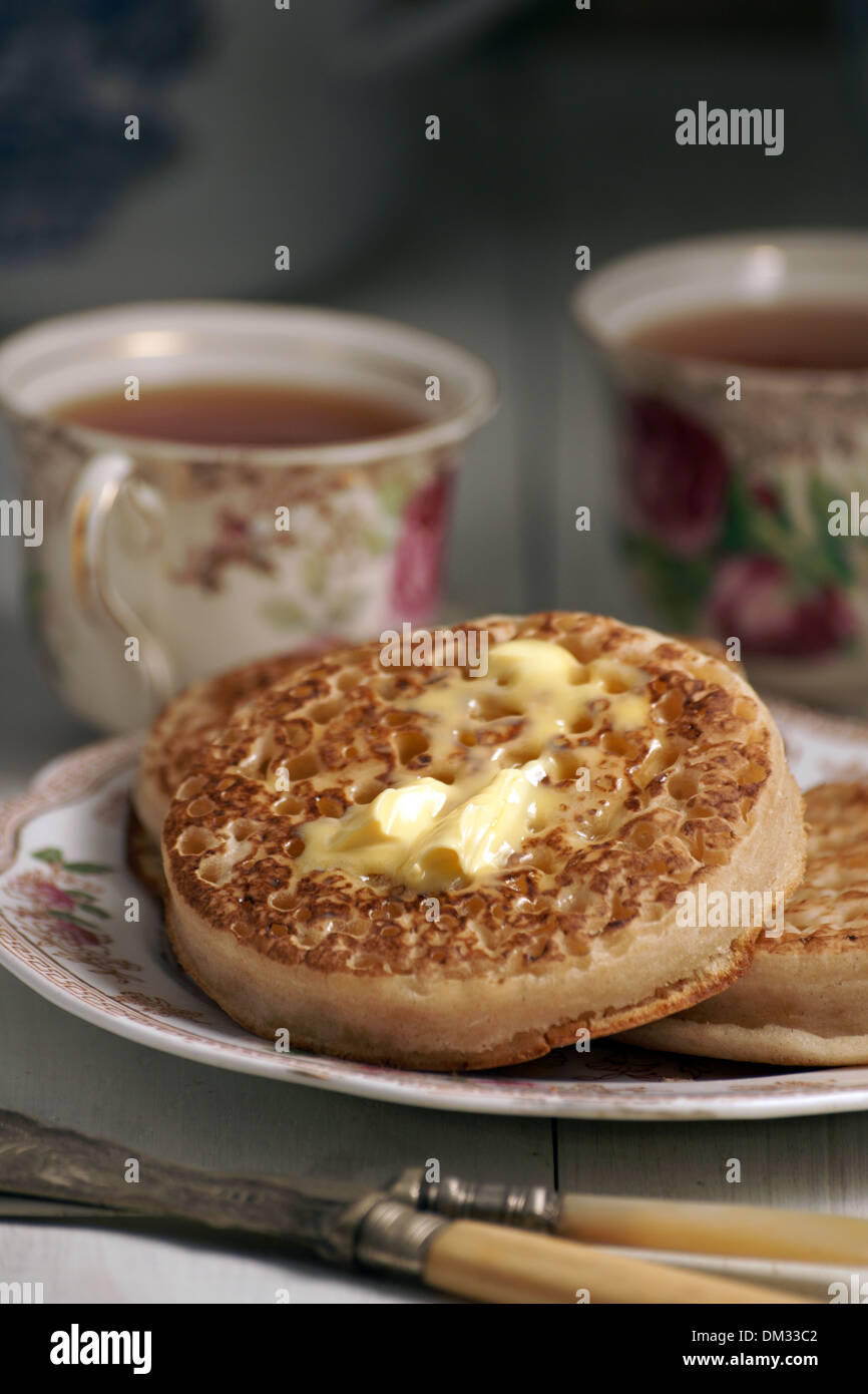 Toasted crumpets with melting butter and tea in floral cups with a vintage feel Stock Photo
