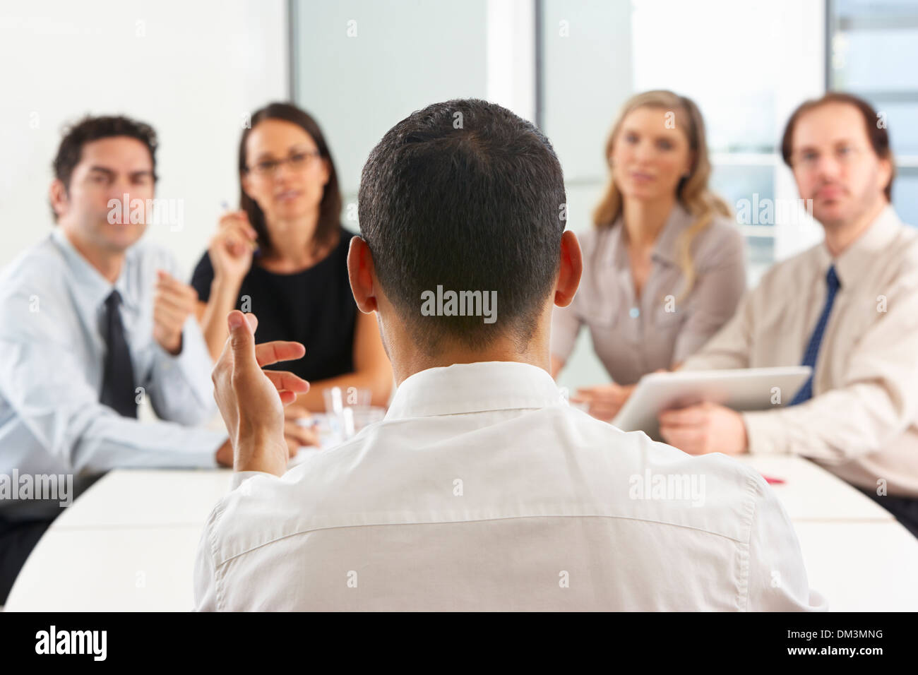 View From Behind As CEO Addresses Meeting In Boardroom Stock Photo