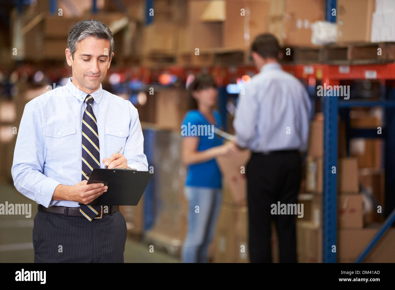 Manager In Warehouse Writing On Clipboard Stock Photo