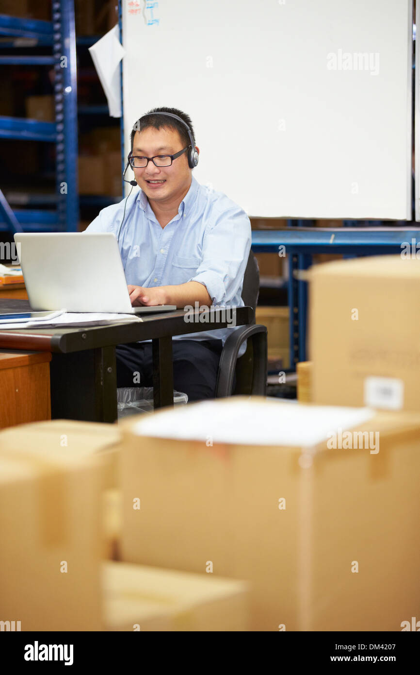 Worker In Warehouse Wearing Headset And Using Laptop Stock Photo