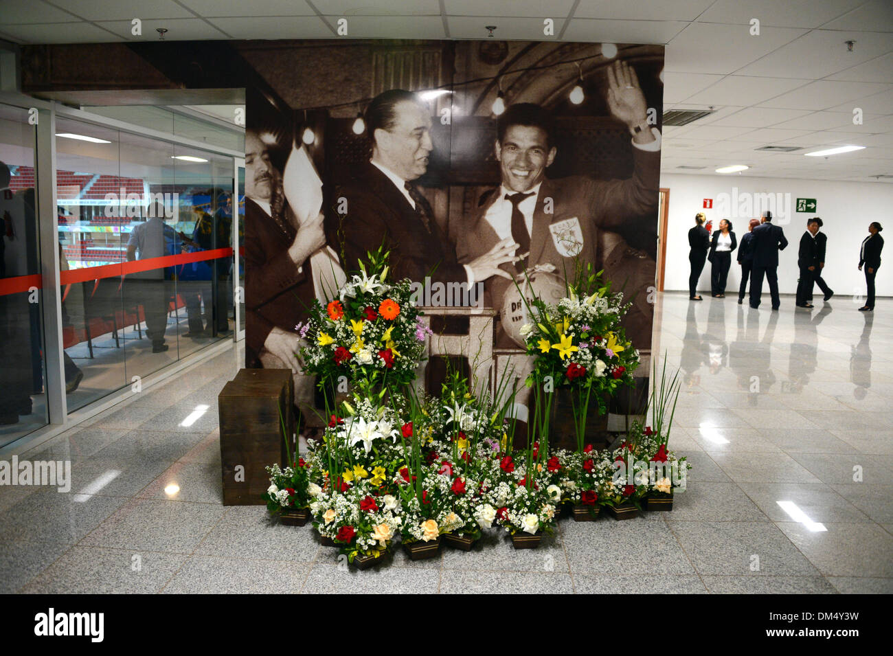 Brasilia, Brazil. 9th Dec, 2013. Flowers lie in front of a large photograph of late Brazilian national soccer player and two-times world champion Mane Garrincha (R) in the lobby area of the 'Stadion Nacional Mane Garrincha' stadium in Brasilia, Brazil, 9 December 2013. The Stadion Nacional Mane Garrincha is one of the venues which will host the matches for the 2014 Soccer World Cup in Brazil. Photo: Marcus Brandt/dpa/Alamy Live News Stock Photo