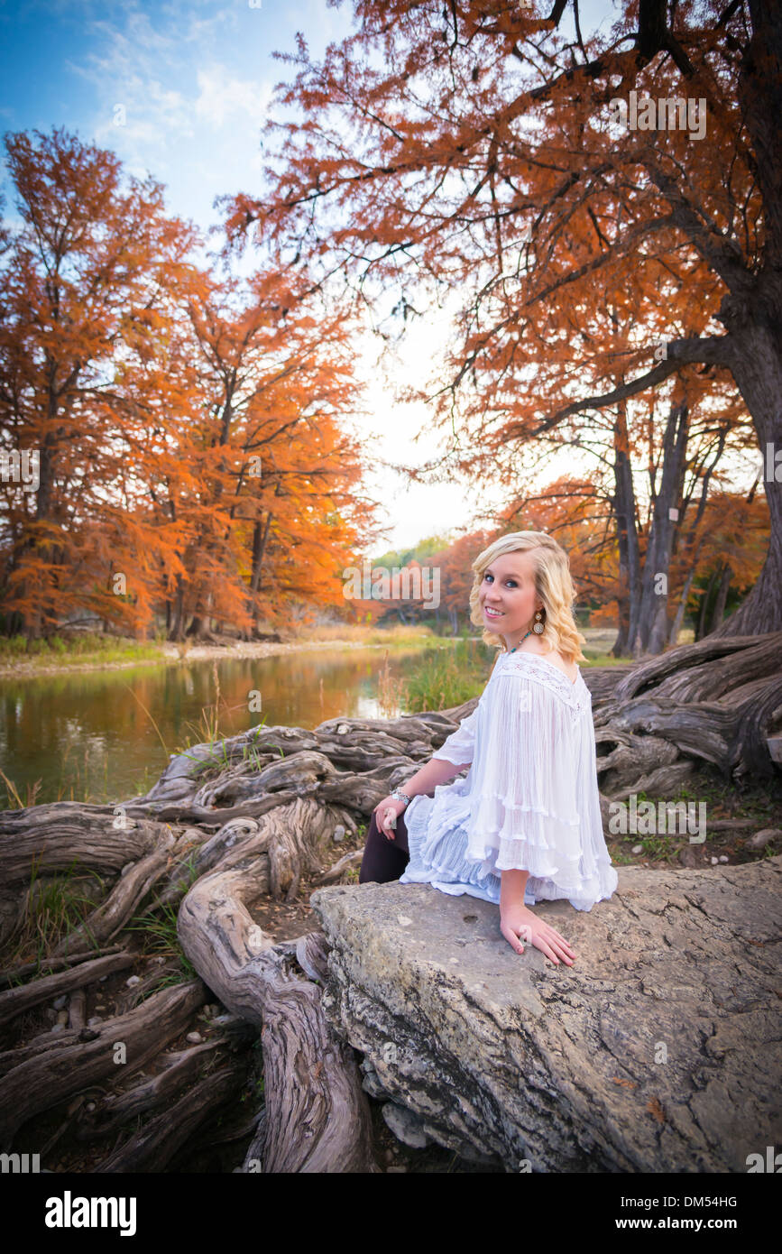 A female caucasian teenager is sitting on a rock next to Cypress tree roots and enjoying nature at the Frio River. Stock Photo