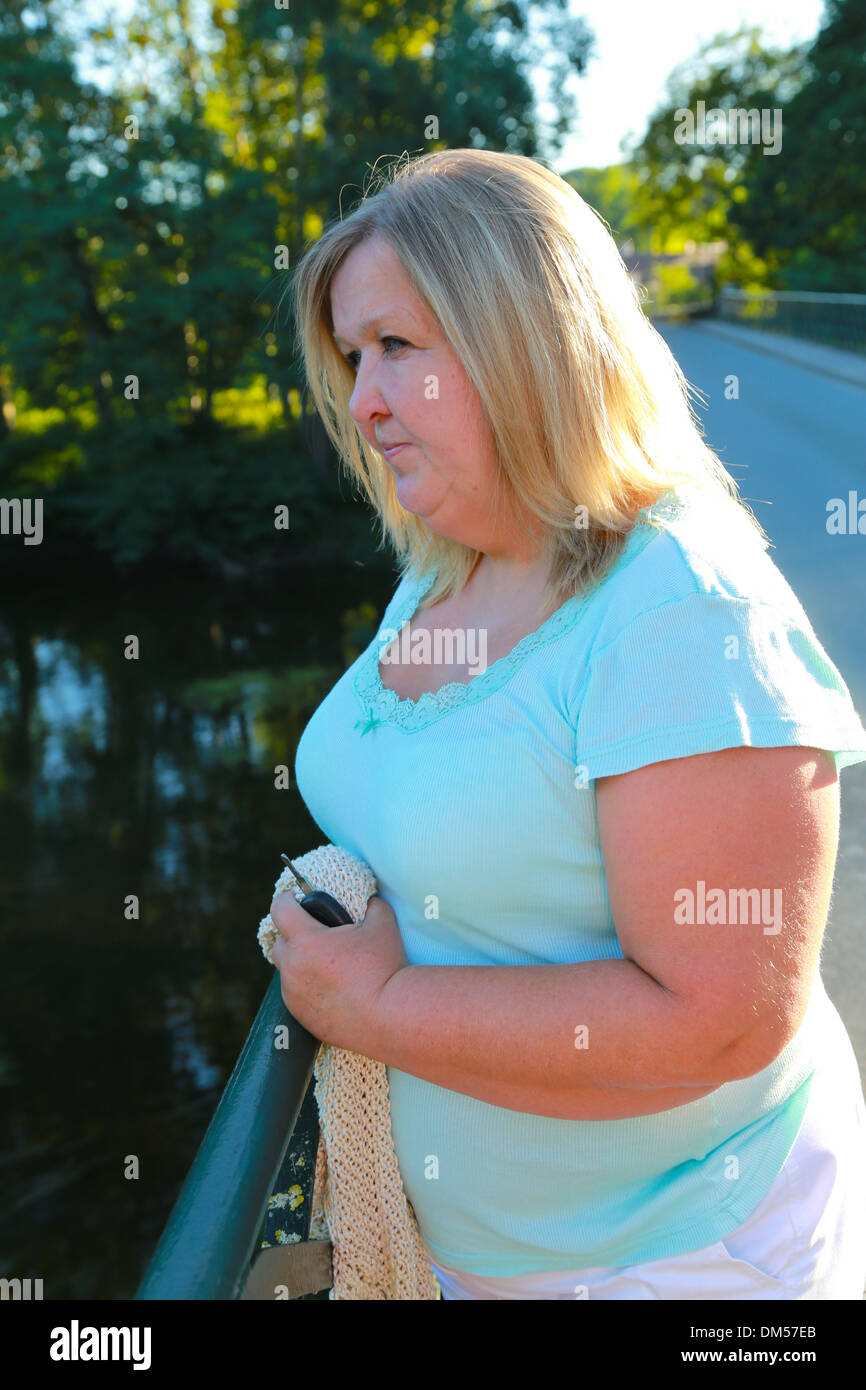 Overweight woman holding car keys, depressed, on a bridge. Stock Photo