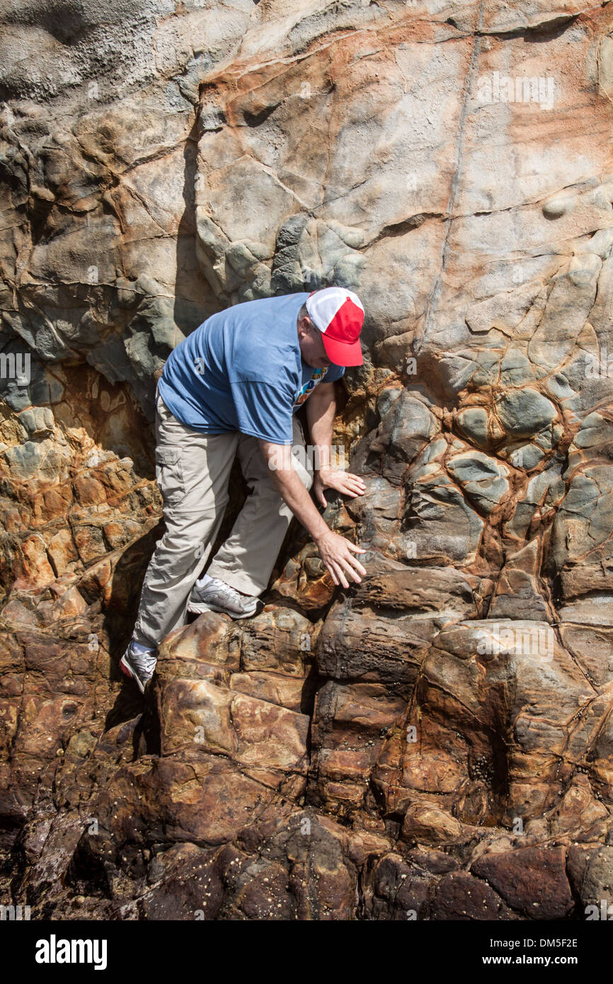 Careful Climbing -vertical orientation of adult man free climbing a steep rock wall in daylight, with copy space Stock Photo