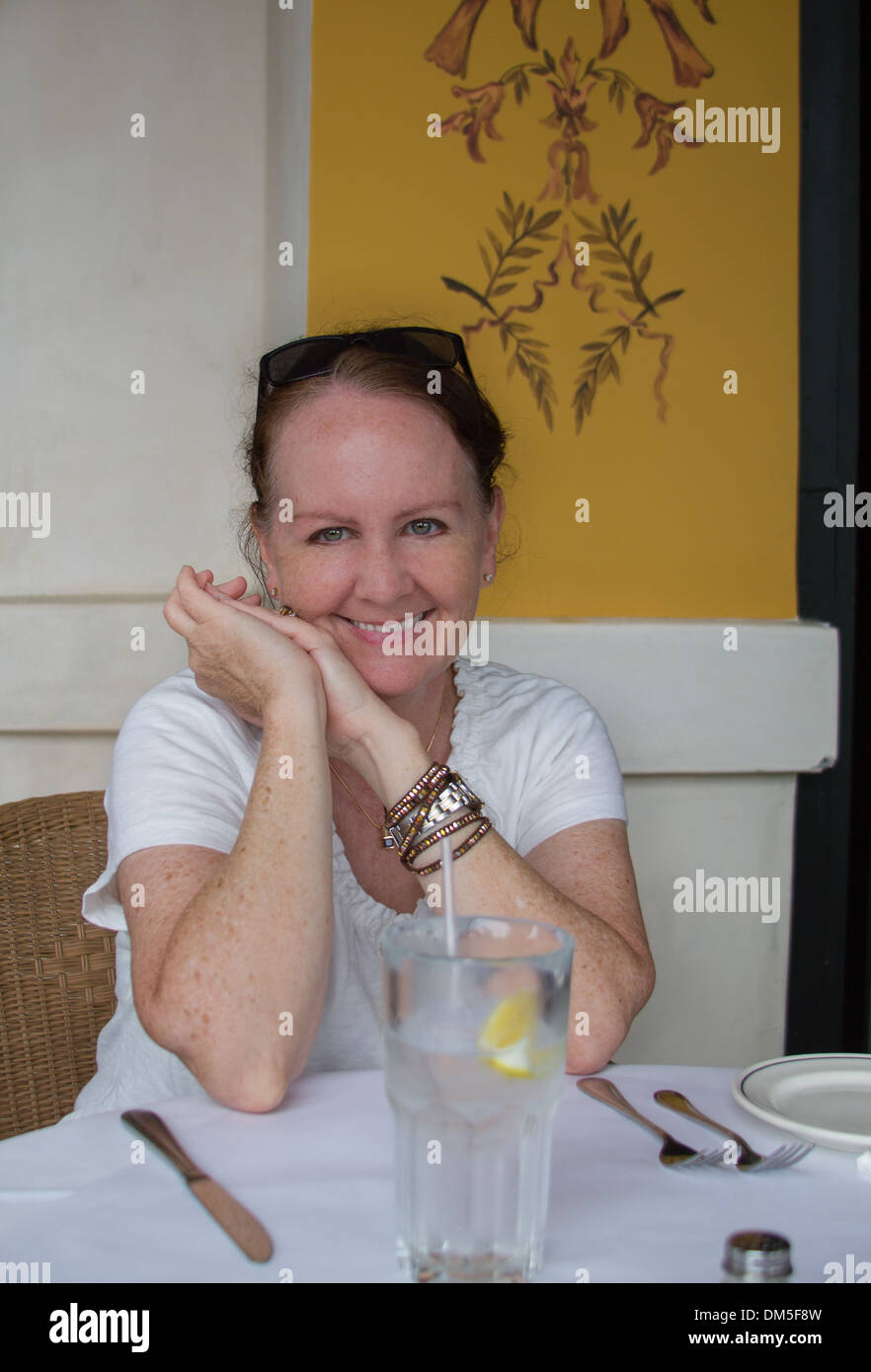 Woman With Water Glass Waits for food - vertical orientation of a single happy, smiling woman with a glass of water with lemon Stock Photo