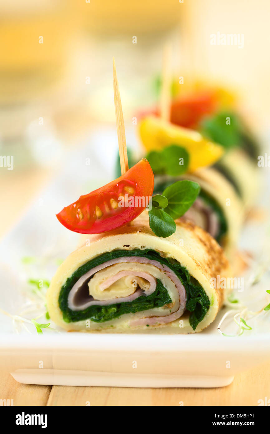Crepe rolls as finger food filled with spinach and ham garnished with cherry tomato and watercress Stock Photo