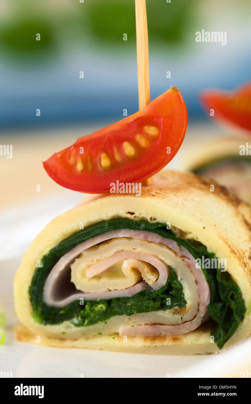 Crepe roll as finger food filled with spinach and ham garnished with cherry tomato Stock Photo