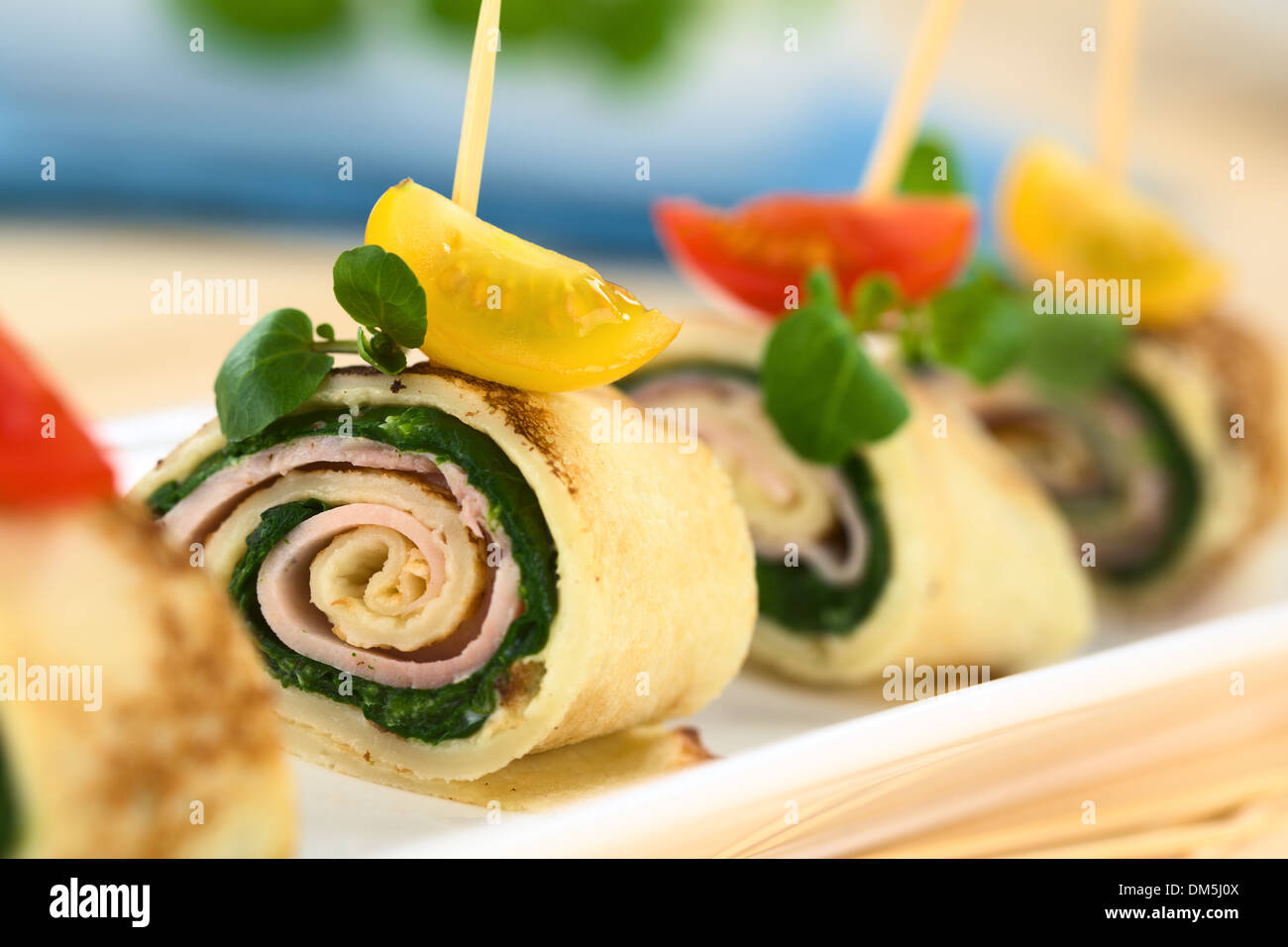 Crepe rolls as finger food filled with spinach and ham garnished with cherry tomato and watercress Stock Photo
