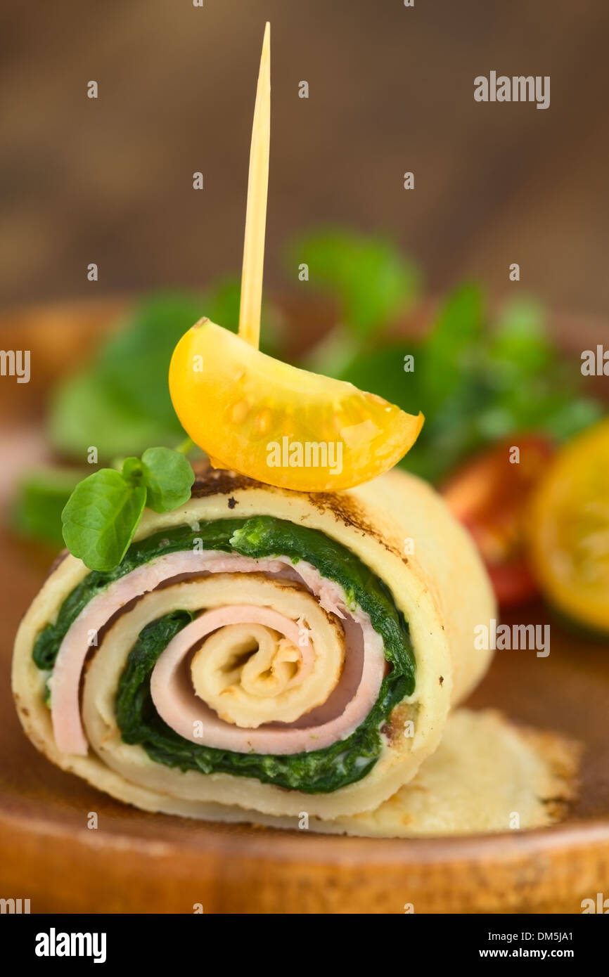 Crepe roll as finger food filled with spinach and ham garnished with cherry tomato and watercress served on wooden plate Stock Photo