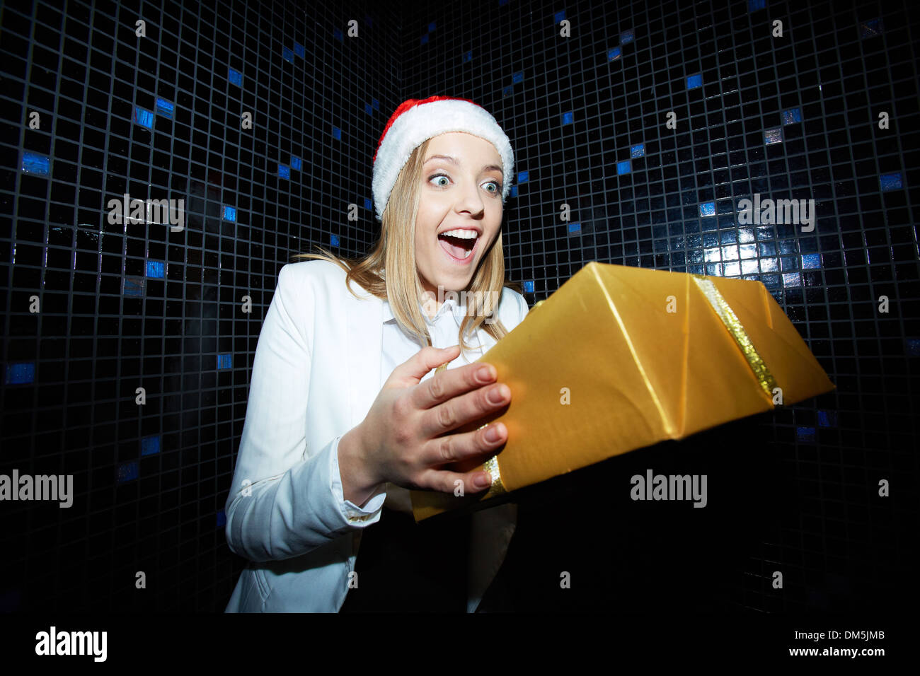 Portrait of pretty businesswoman in Santa cap looking at Chistmas gift with gladness Stock Photo