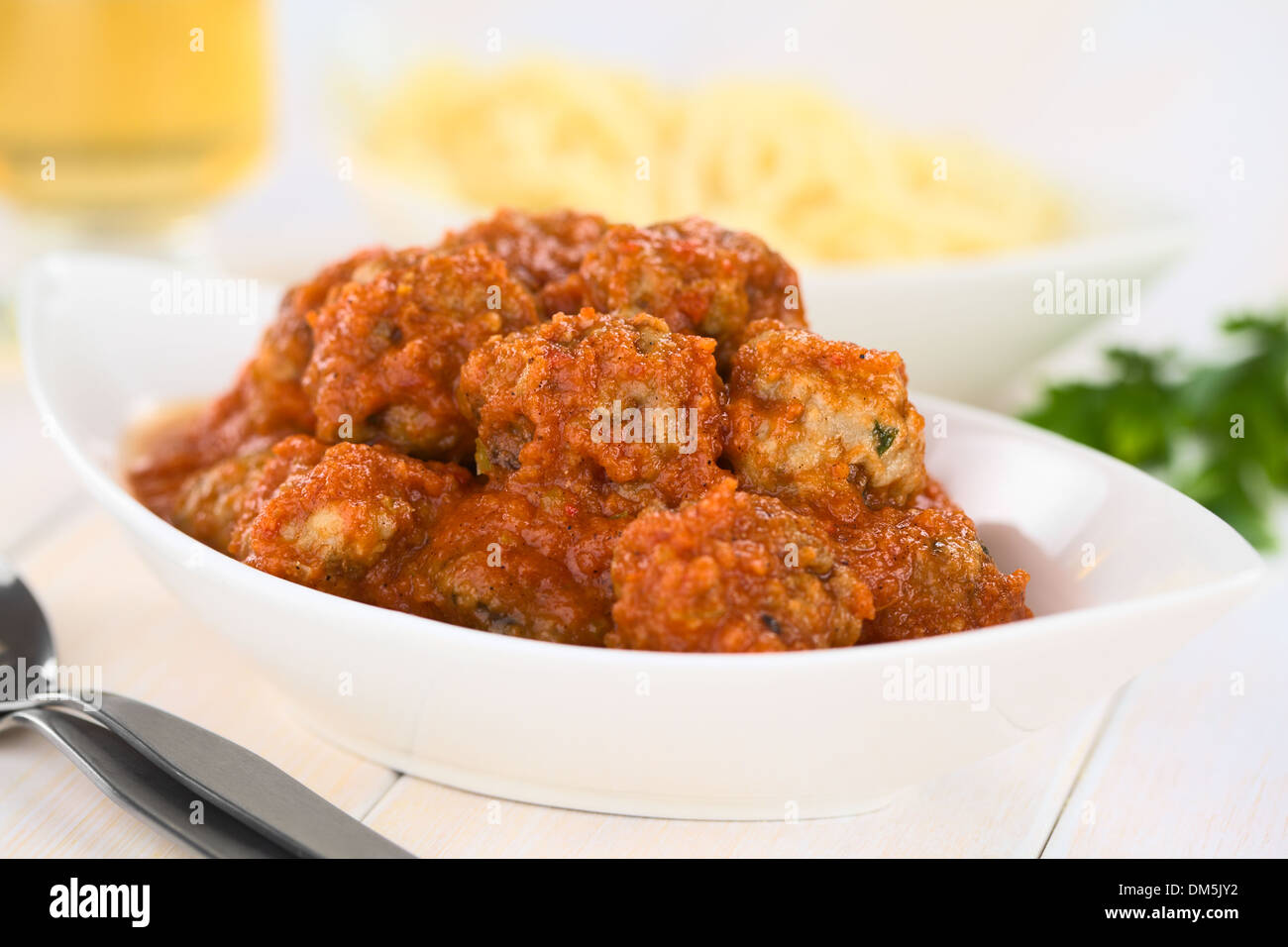 Spanish albondigas (meatballs) in tomato sauce in bowl with spaghetti and white wine in the back Stock Photo