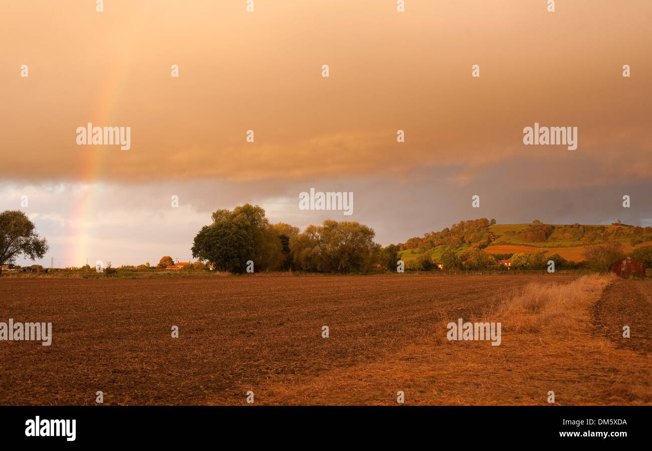 Looking towards Meon Hill over farmland with a dramatic sunset and rainbow, Gloucestershire, England. Stock Photo