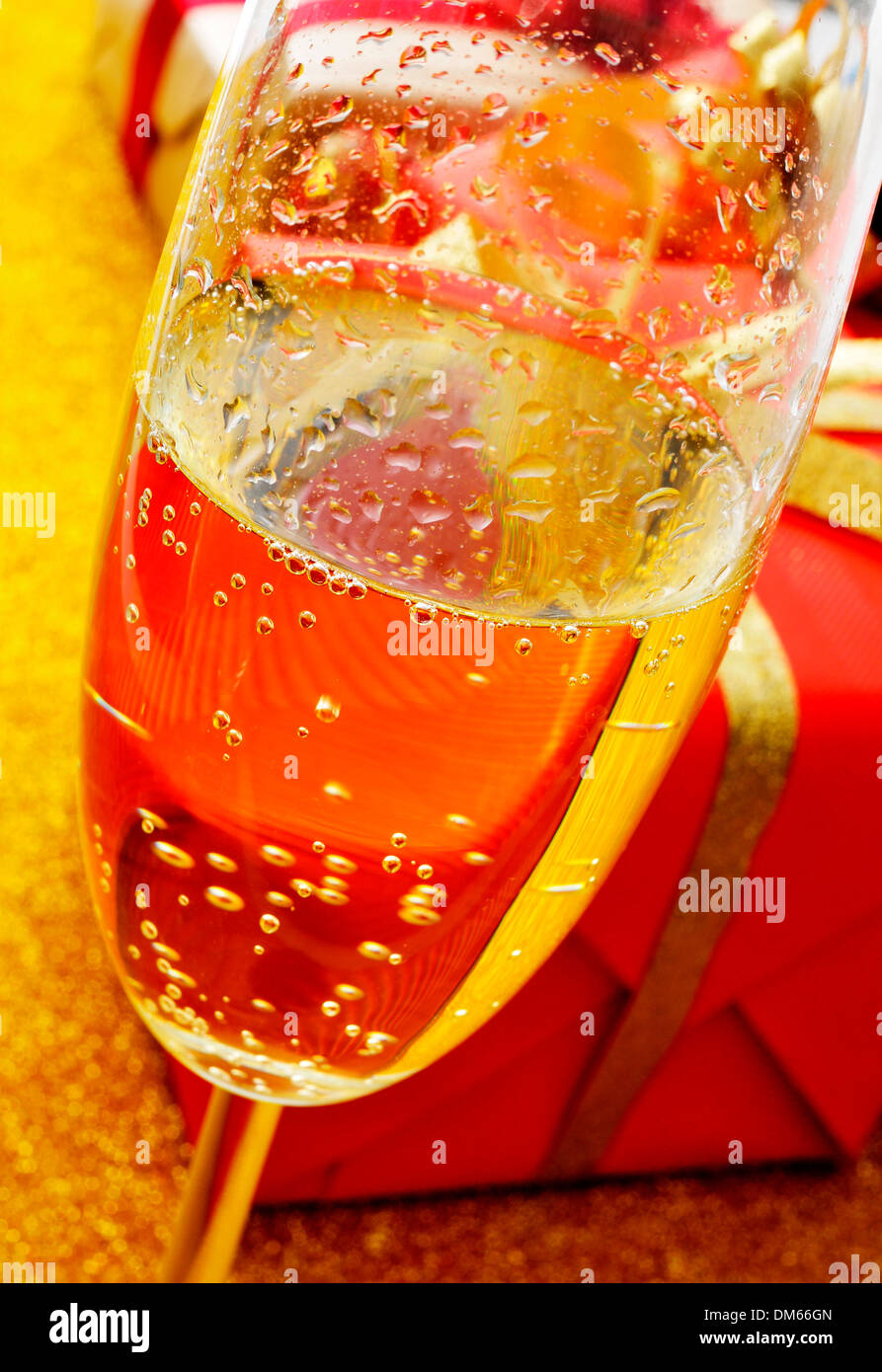 a glass with champagne and some gifts on a golden background Stock Photo