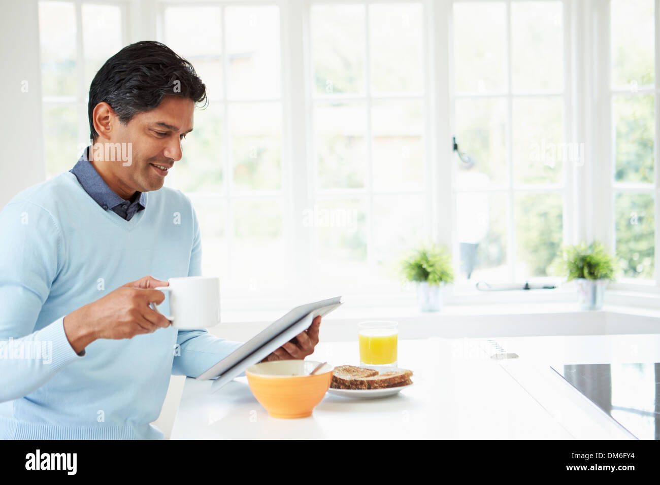 Indian Man Using Digital Tablet Whilst Eating Breakfast Stock Photo